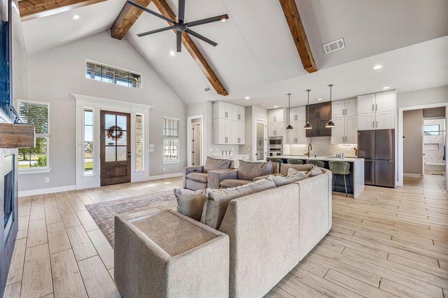 Living area featuring high vaulted ceiling, ceiling fan, beamed ceiling, light wood-style flooring, and a fireplace