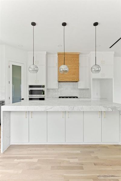 Kitchen with light hardwood / wood-style flooring, oven, decorative light fixtures, and tasteful backsplash