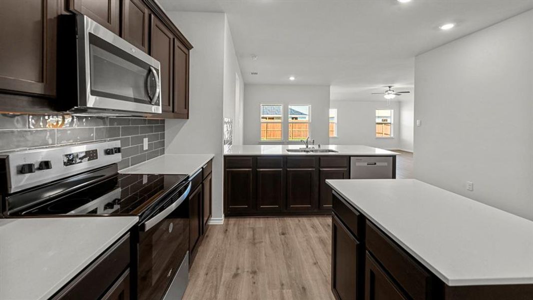 Kitchen with stainless steel appliances, recessed lighting, dark wood finish cabinetry, light wood-type flooring, and a peninsula