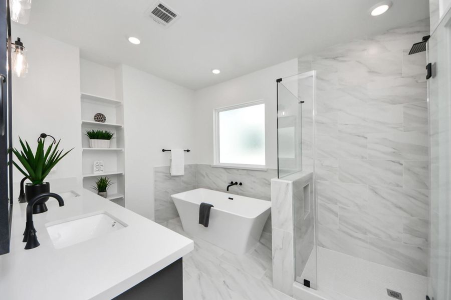 This bathroom features a modern design with a freestanding bathtub, a glass-enclosed shower, and elegant marble-like tiles. It includes a spacious countertop with a sleek sink and black fixtures, complemented by built-in shelving for storage. The large frosted window provides ample natural light while maintaining privacy. This bathroom features a modern design with a freestanding bathtub, a glass-enclosed shower, and elegant marble-like tiles. It includes a spacious countertop with a sleek sink and black fixtures, complemented by built-in shelving for storage. The large frosted window provides ample natural light while maintaining privacy.
