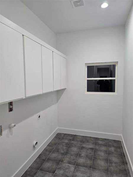 Laundry area featuring dark tile patterned floors, hookup for a washing machine, electric dryer hookup, and cabinets