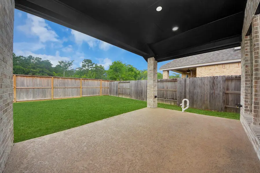 This photo shows a covered patio with a concrete floor, overlooking a well-maintained grassy backyard enclosed by a wooden fence, providing a private and inviting outdoor space.