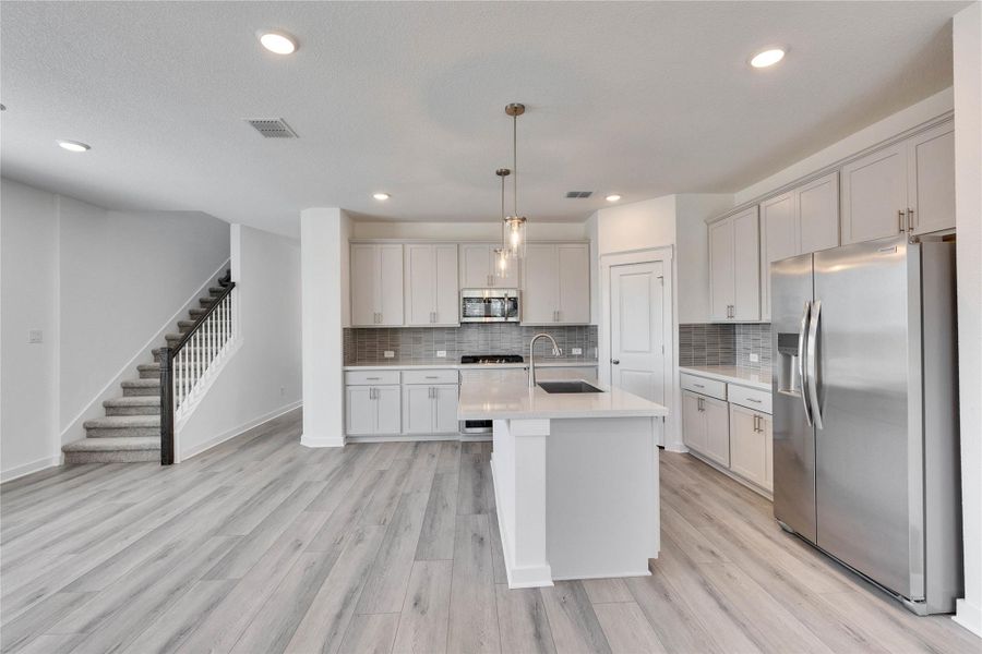 Kitchen with stainless steel appliances, pendant lighting, light wood-style floors, backsplash, and an island with sink