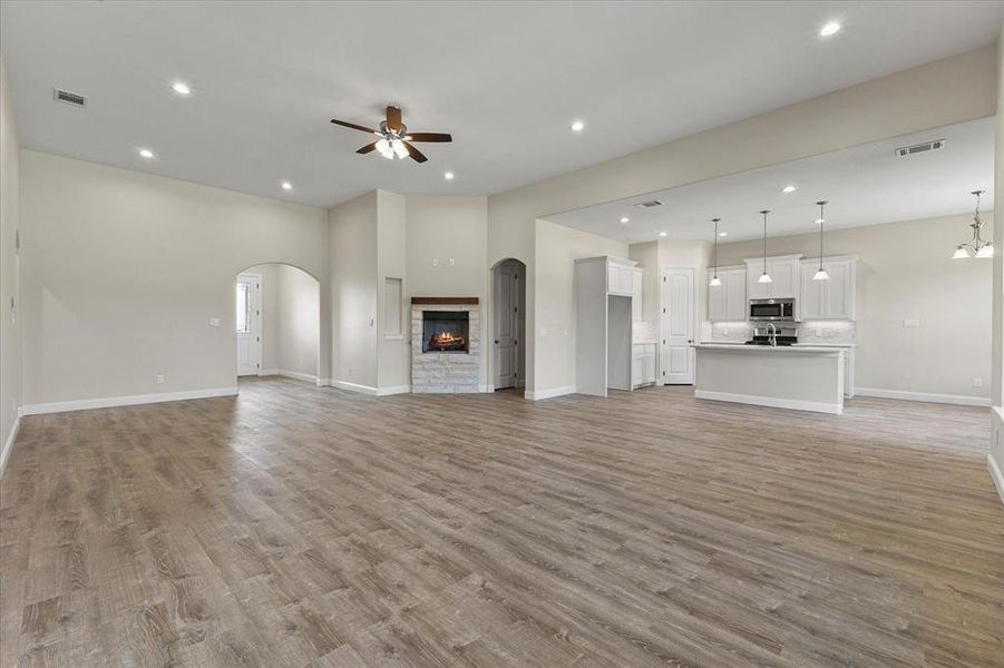 Unfurnished living room with a ceiling fan, light wood-style flooring, recessed lighting, a stone fireplace, and arched walkways