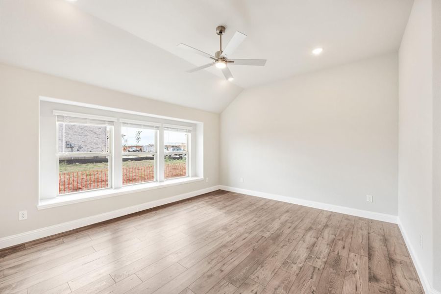 Empty room with vaulted ceiling, ceiling fan, hardwood floors, and large triple window Empty room with vaulted ceiling, ceiling fan, hardwood floors, and large triple window
