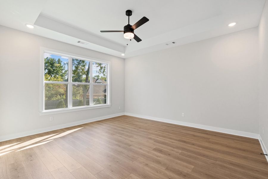 Tray ceiling with recessed lighting, large multi-pane window, wood-finish flooring, and a ceiling fan with integrated lighting Tray ceiling with recessed lighting, large multi-pane window, wood-finish flooring, and a ceiling fan with integrated lighting