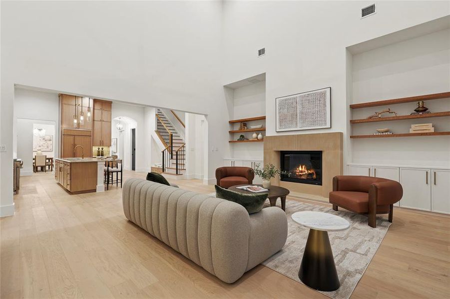 Living room featuring built in features, light wood finished floors, stairway, a glass covered fireplace, and a towering ceiling