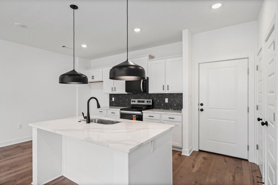 Kitchen featuring a white quartz-finish island, black pendant lighting, white cabinetry, and a dark tile backsplash Kitchen featuring a white quartz-finish island, black pendant lighting, white cabinetry, and a dark tile backsplash