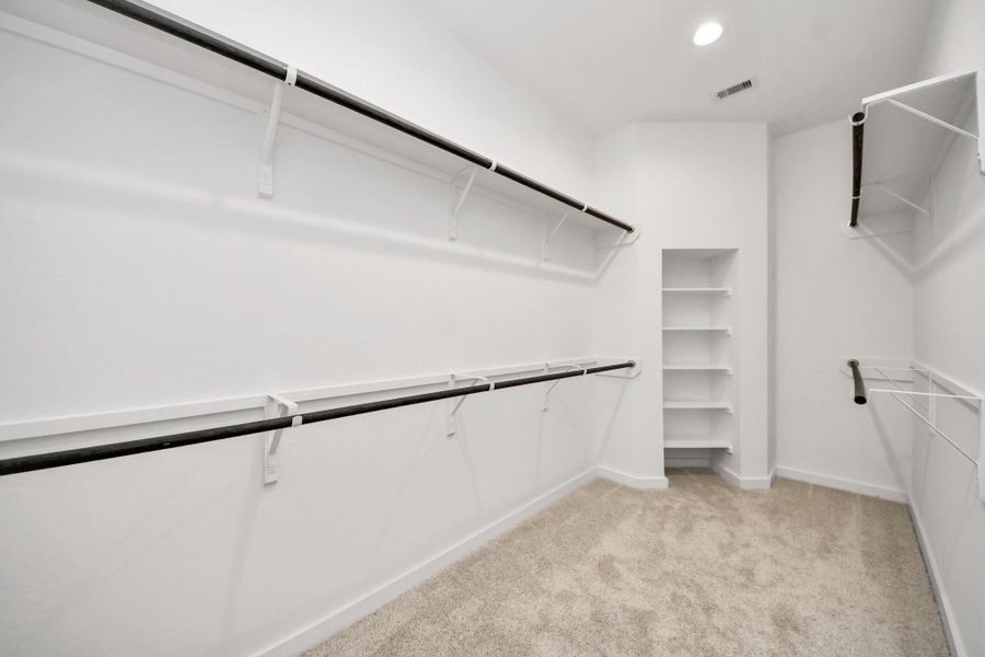 Walk-in closet that epitomizes luxury and practicality. This generously sized space features built-in shelving, offering abundant room for impeccable organization. High ceilings and recessed lighting create a bright and welcoming ambiance. Sample photo of completed home with similar floor plan. Actual colors and selections may vary.