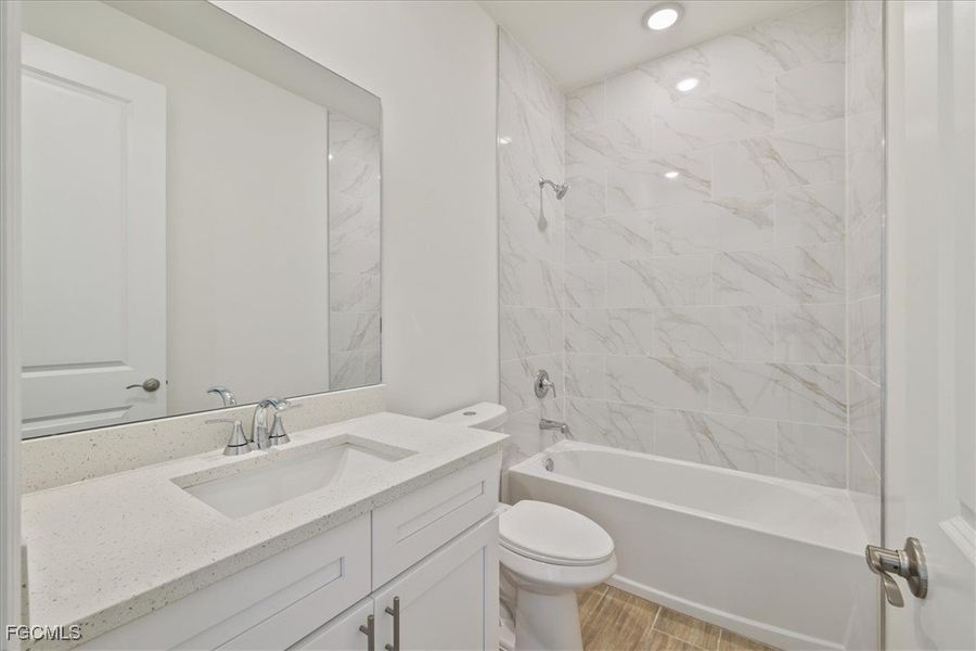 Bathroom with washtub / shower combination, vanity, and light wood-style floors