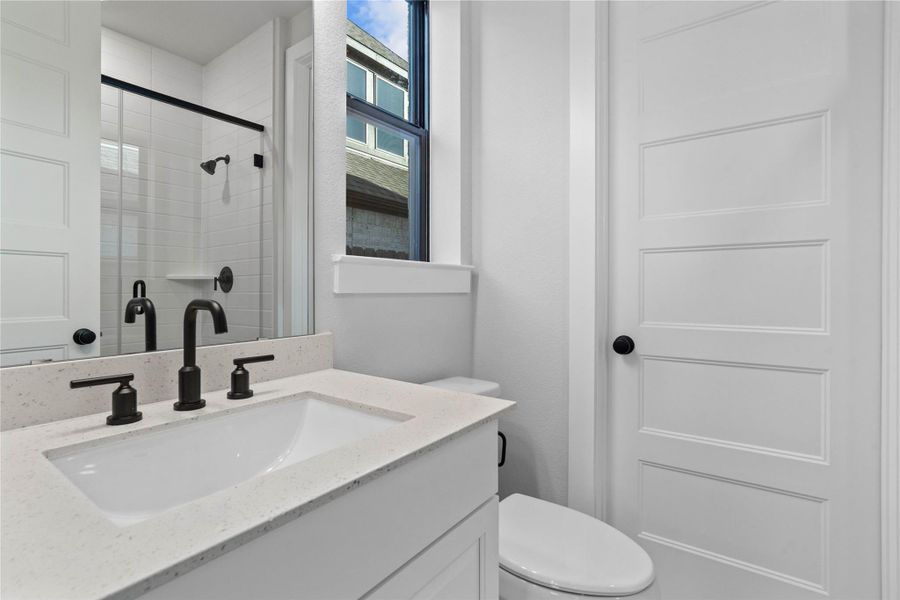This ensuite secondary bathroom features a modern vanity, large framed walk-in shower, window, and matte black  finishes.
