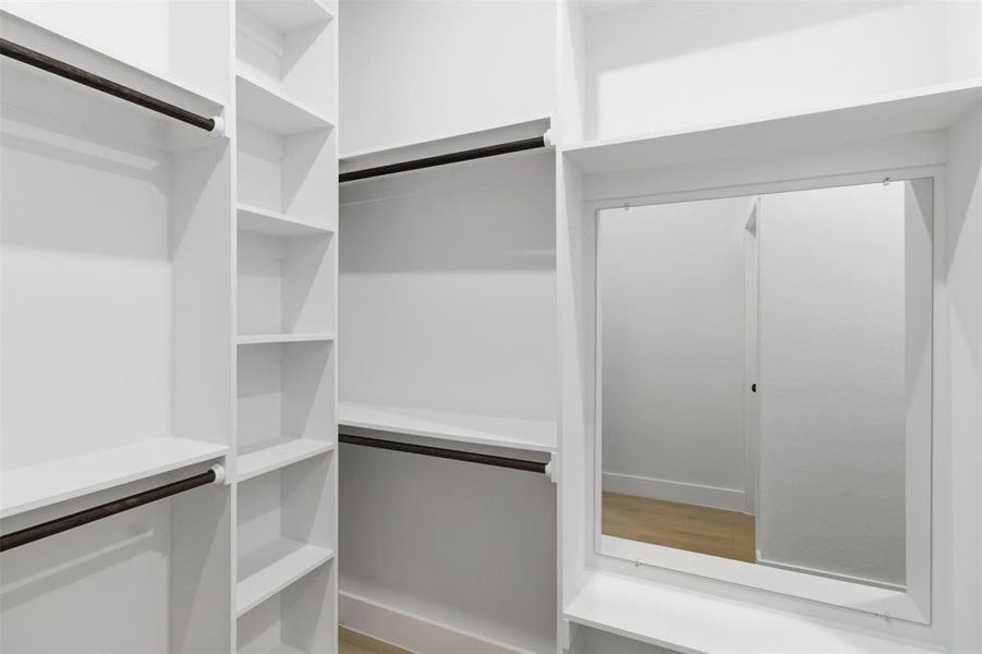 Custom closet system featuring white shelving, multiple hanging rods, and an integrated mirror