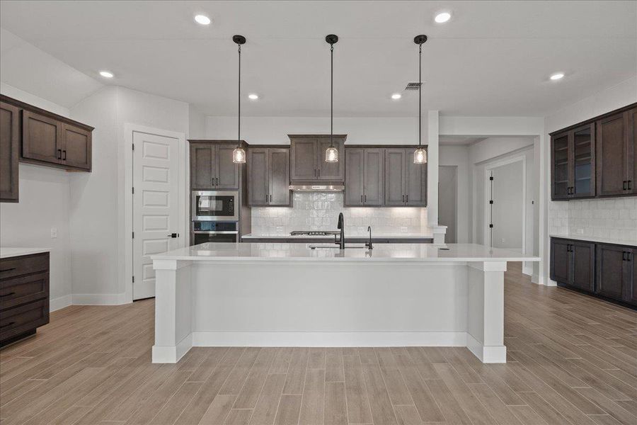 Kitchen featuring dark brown cabinets, hanging light fixtures, a kitchen bar, light wood finished floors, and recessed lighting Kitchen featuring dark brown cabinets, hanging light fixtures, a kitchen bar, light wood finished floors, and recessed lighting