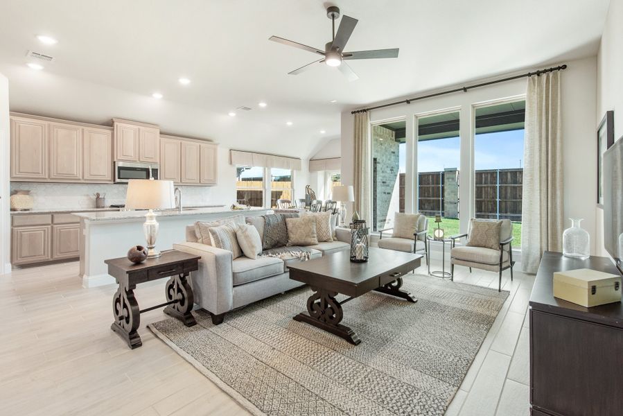 Open-concept living room and kitchen with gray sofa, ceiling fan, large windows, and tan cabinets with granite island Open-concept living room and kitchen with gray sofa, ceiling fan, large windows, and tan cabinets with granite island