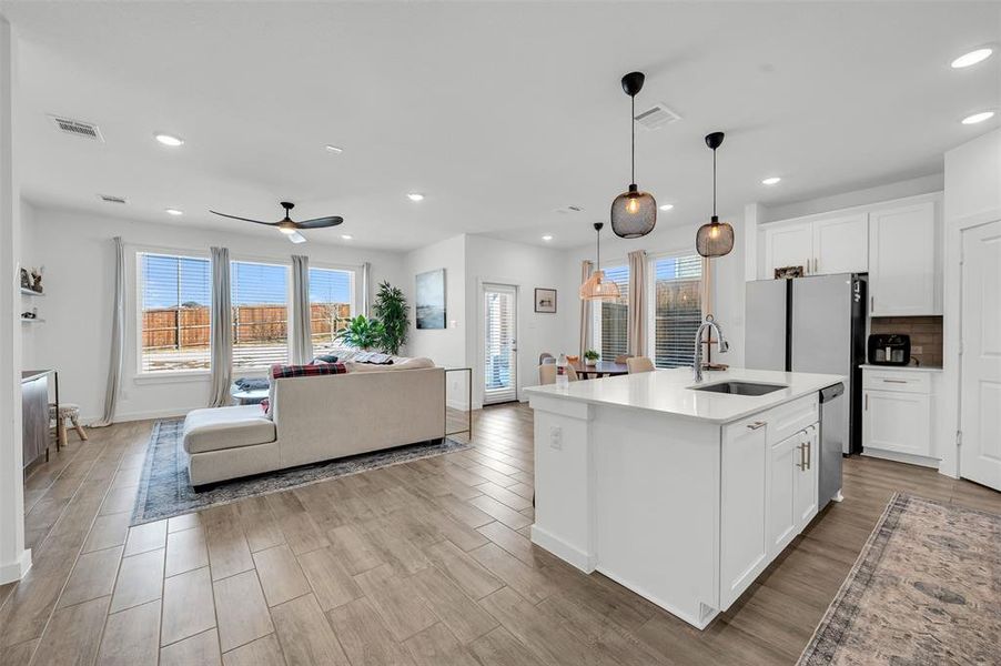 Kitchen with a kitchen island with sink, sink, pendant lighting, and white cabinets