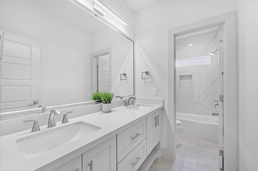 This is a modern, bright bathroom featuring a double vanity with sleek fixtures, a large wall mirror, and contemporary lighting. The room leads to a shower/tub combo with elegant tile work, creating a clean and inviting space. This is a modern, bright bathroom featuring a double vanity with sleek fixtures, a large wall mirror, and contemporary lighting. The room leads to a shower/tub combo with elegant tile work, creating a clean and inviting space.