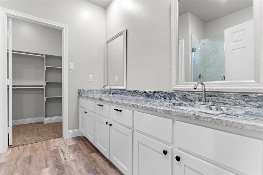 Bathroom featuring double vanity, a stall shower, wood finished floors, baseboards, and a spacious closet Bathroom featuring double vanity, a stall shower, wood finished floors, baseboards, and a spacious closet
