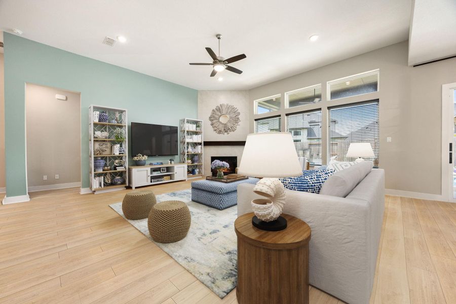 This spacious living area showcases soaring ceilings, recessed lighting, and expansive windows that fill the room with natural light. The sleek fireplace creates a warm focal point, while the light wood-style flooring enhances the open and inviting atmosphere. A perfect blend of comfort and style, this space is ideal for both everyday living and entertaining.