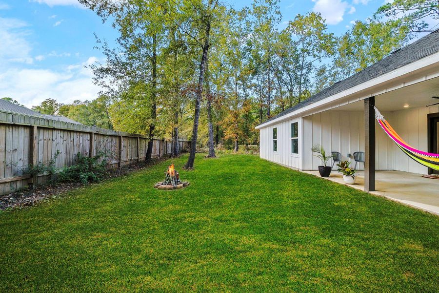 This photo showcases a spacious backyard featuring a well-maintained lawn and a covered patio with a hammock. The area is fenced and bordered by trees, offering privacy and a serene outdoor space.