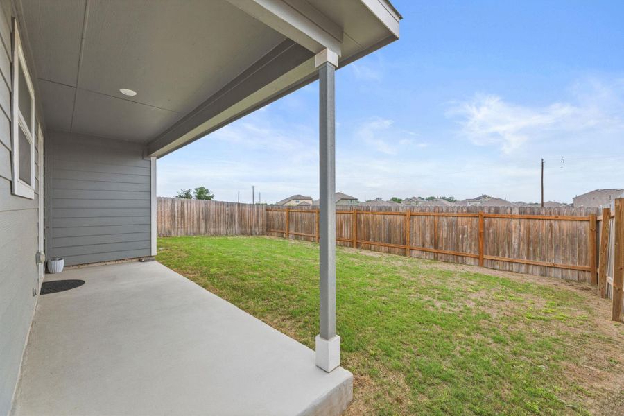 The property features a covered patio with a concrete surface, a well-maintained lawn, and a wooden fence enclosing the yard