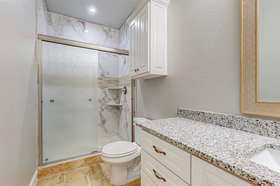 Bathroom featuring a shower with shower door, vanity, tile patterned floors, and toilet