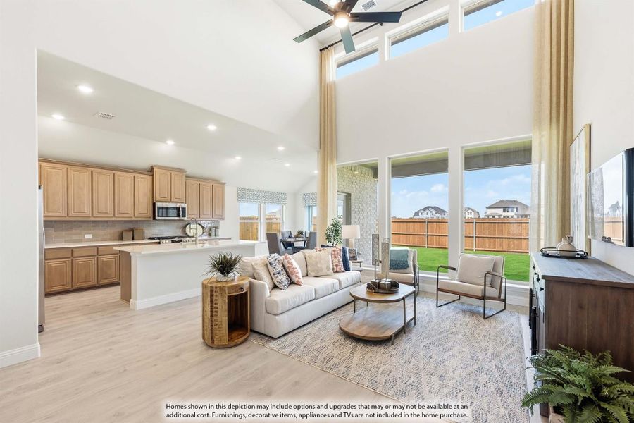 Open-concept living room with two-story ceiling, ceiling fan, and view into kitchen with wood cabinets