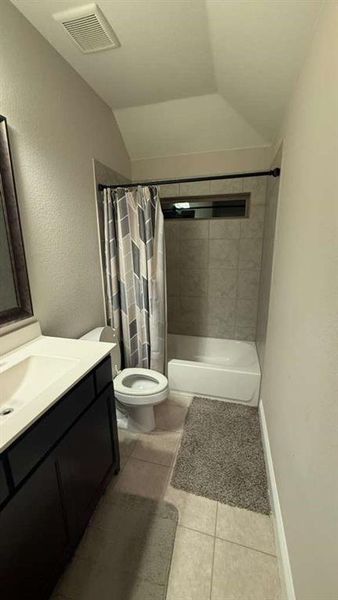 Full bathroom featuring vanity, shower / bathtub combination with curtain, light tile patterned floors, lofted ceiling, and a textured wall