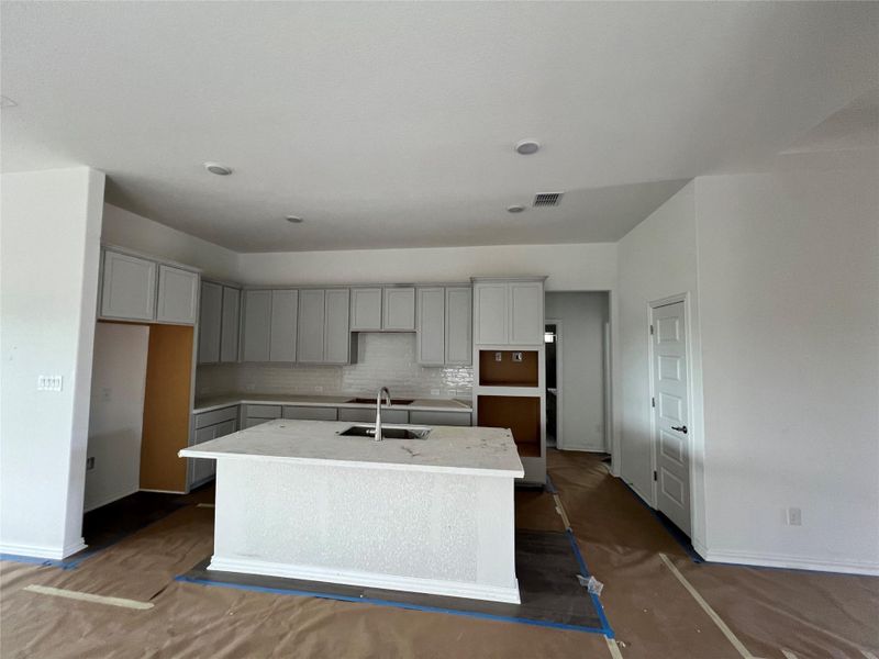 Kitchen with a kitchen island with sink, decorative backsplash, and gray cabinetry Kitchen with a kitchen island with sink, decorative backsplash, and gray cabinetry