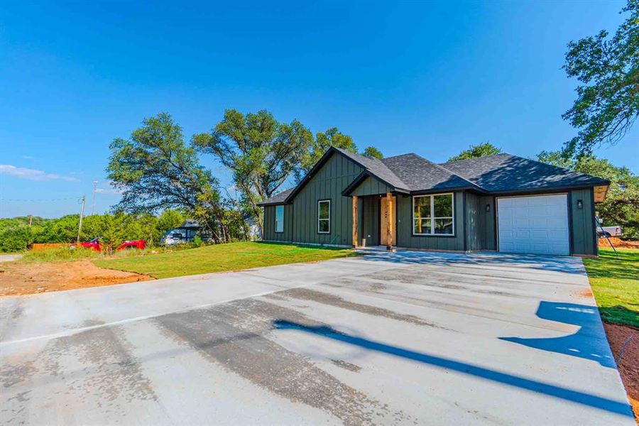 View of front of home featuring a front lawn, concrete driveway, an attached garage, board and batten siding, and roof with shingles