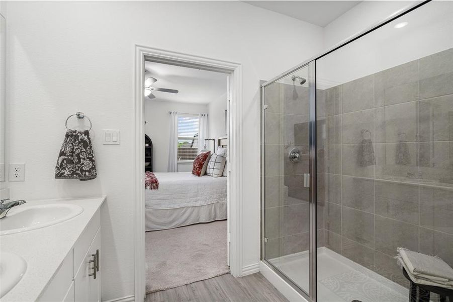 Bathroom featuring a glass-enclosed shower with gray tiled walls and a double vanity with white countertops and white cabinetry