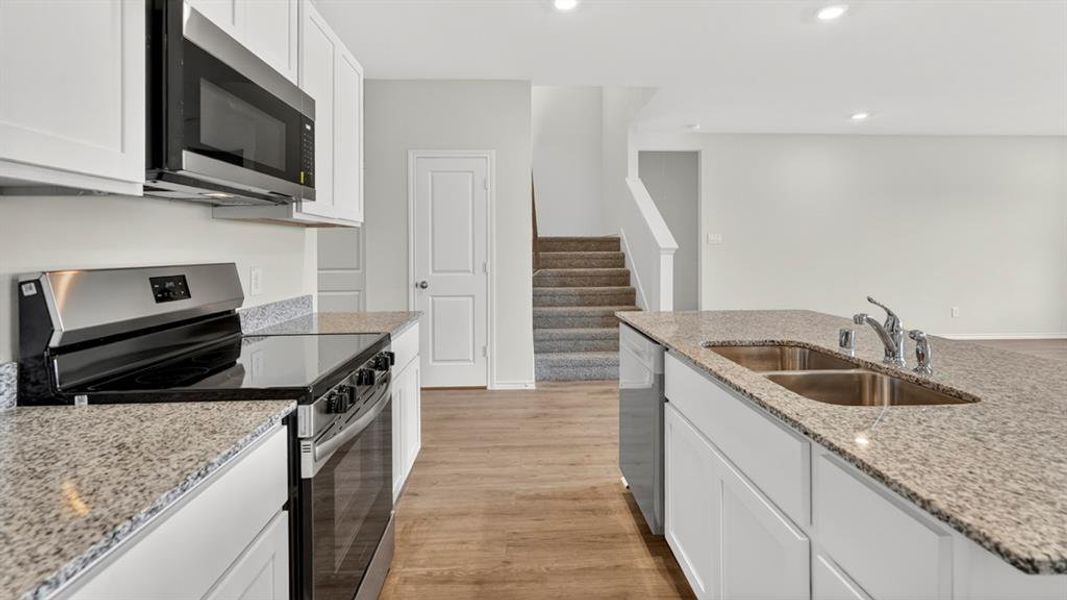 Modern kitchen featuring an island with a double basin sink, stainless steel appliances, granite countertops, white cabinetry, and wood-finish flooring