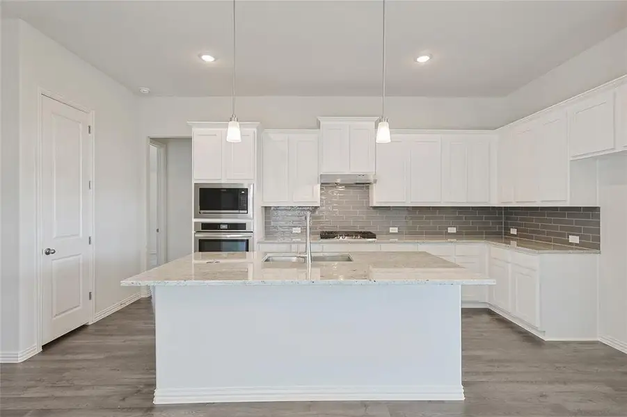 Kitchen with light stone countertops, an island with sink, white cabinets, stainless steel appliances, and light wood-style flooring