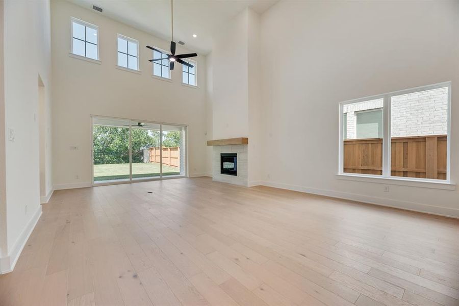 Unfurnished living room featuring a towering ceiling, a tile fireplace, light wood-type flooring, and a ceiling fan Unfurnished living room featuring a towering ceiling, a tile fireplace, light wood-type flooring, and a ceiling fan