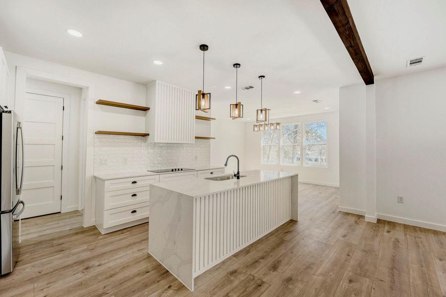 Kitchen with a kitchen island with sink, open shelves, light stone counters, decorative light fixtures, and freestanding refrigerator
