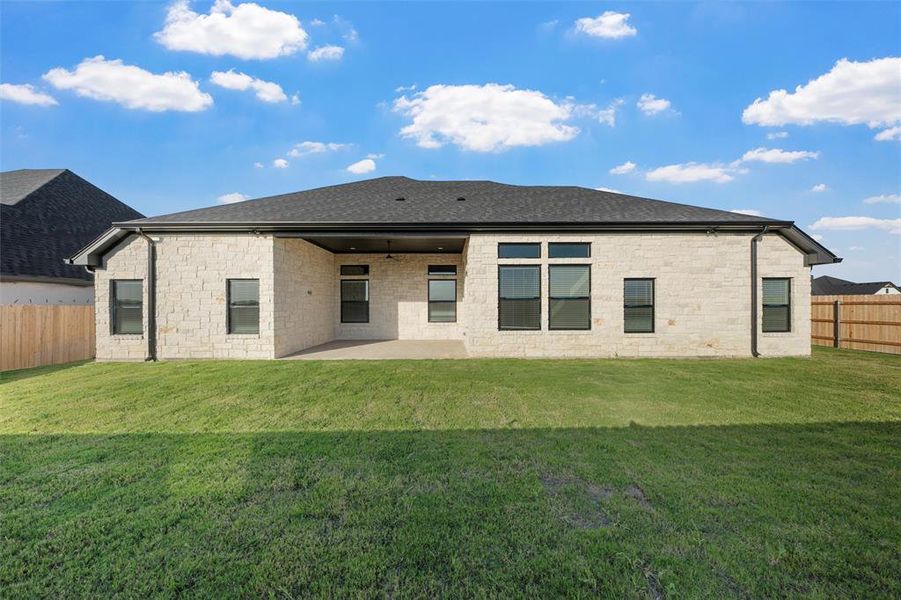 Rear view of house with a patio area, roof with shingles, and stone siding Rear view of house with a patio area, roof with shingles, and stone siding
