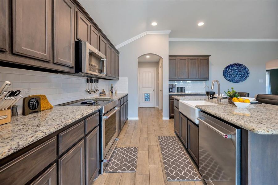 Kitchen with arched walkways, crown molding, stainless steel appliances, tasteful backsplash, and light stone counters