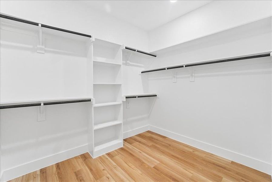 Walk-in closet featuring light wood-finish flooring, white walls, built-in shelving, and multiple clothing rods Walk-in closet featuring light wood-finish flooring, white walls, built-in shelving, and multiple clothing rods