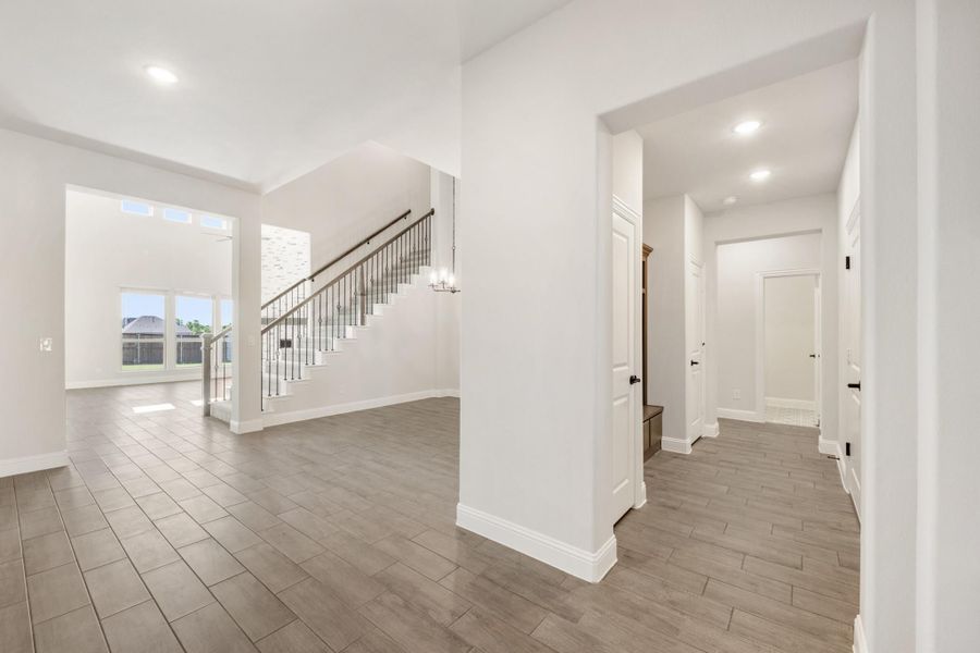 Open home entryway with staircase, wood-look tile floors, and white walls leading to hallway Open home entryway with staircase, wood-look tile floors, and white walls leading to hallway