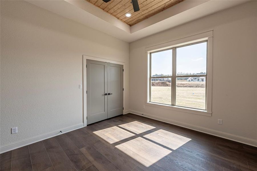 Unfurnished bedroom with a wooden tray ceiling, dark wood-style floors, ceiling fan, and a closet Unfurnished bedroom with a wooden tray ceiling, dark wood-style floors, ceiling fan, and a closet
