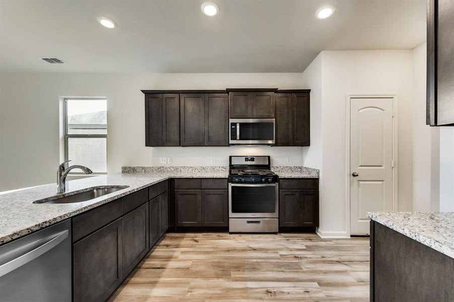 Kitchen with dark cabinets, light wood-type flooring, stainless steel appliances, light stone countertops, and sink