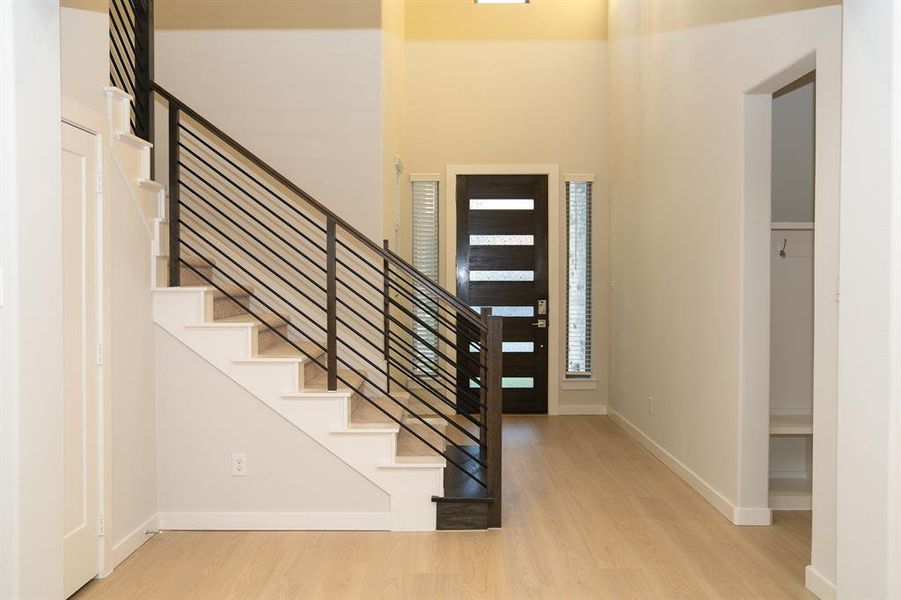 Entryway featuring a modern staircase with dark metal horizontal railings and light wood-finish flooring Entryway featuring a modern staircase with dark metal horizontal railings and light wood-finish flooring