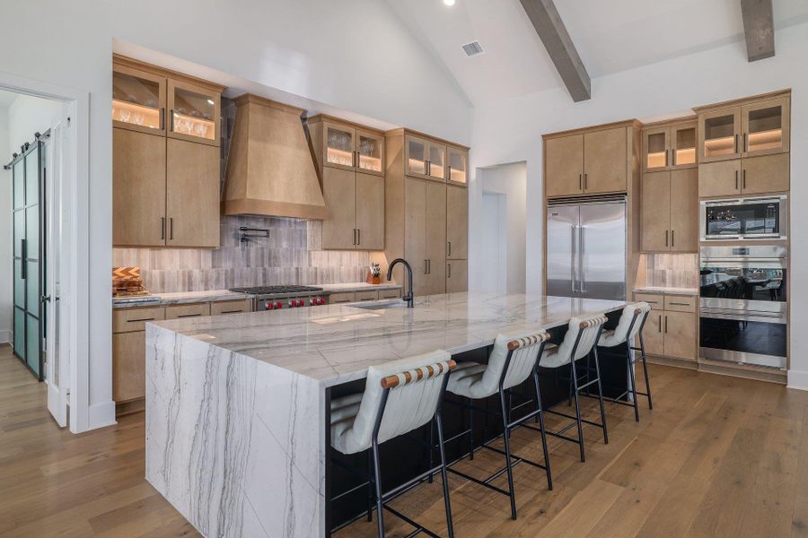 The chef’s kitchen is anchored by a dramatic waterfall-edge island, custom cabinetry, and premium stainless appliances.