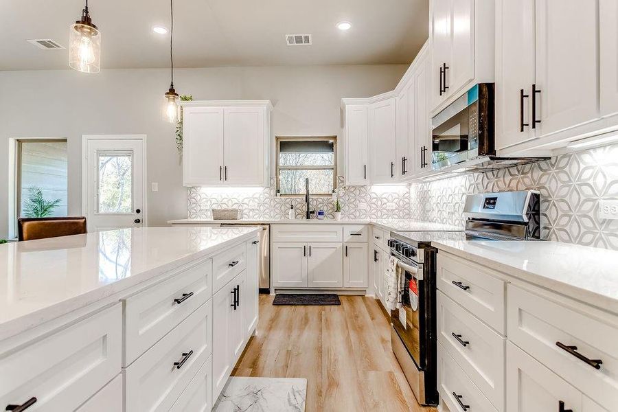 Kitchen with plenty of natural light, white cabinetry, hanging light fixtures, and appliances with stainless steel finishes