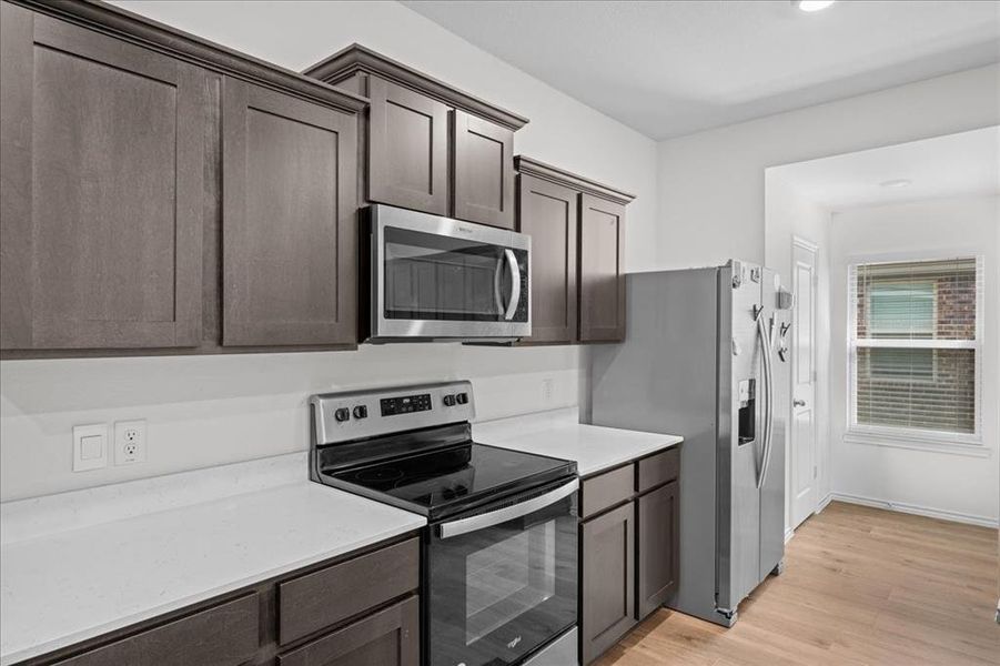 Kitchen featuring stainless steel appliances, light wood-type flooring, dark brown cabinets, light stone countertops, and recessed lighting Kitchen featuring stainless steel appliances, light wood-type flooring, dark brown cabinets, light stone countertops, and recessed lighting