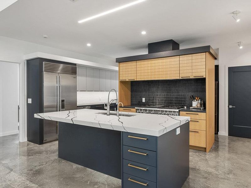 Kitchen featuring decorative backsplash, modern cabinets, built in refrigerator, an island with sink, and light stone countertops