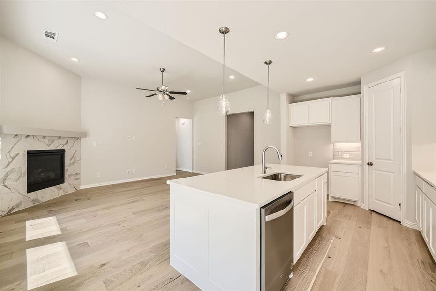 Kitchen featuring white cabinets, a center island with sink, a fireplace, light hardwood / wood-style floors, and sink