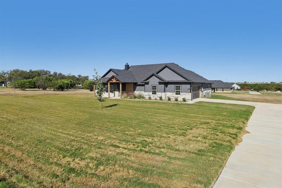 Modern farmhouse style home with a chimney, a front lawn, driveway, stone siding, and an attached garage