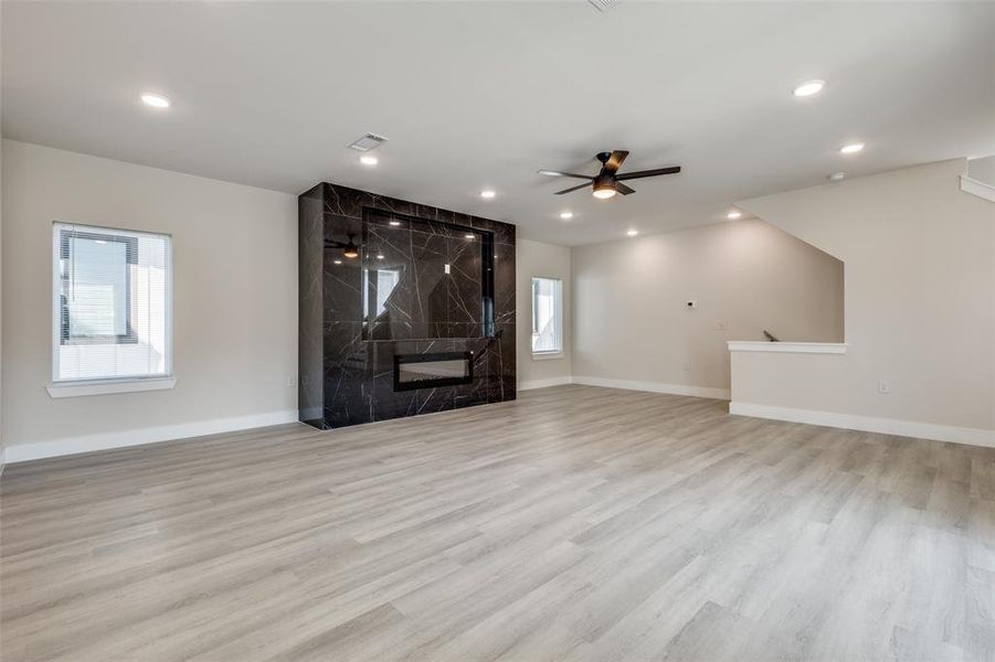 Unfurnished living room featuring a ceiling fan, a high end fireplace, and light wood-style flooring
