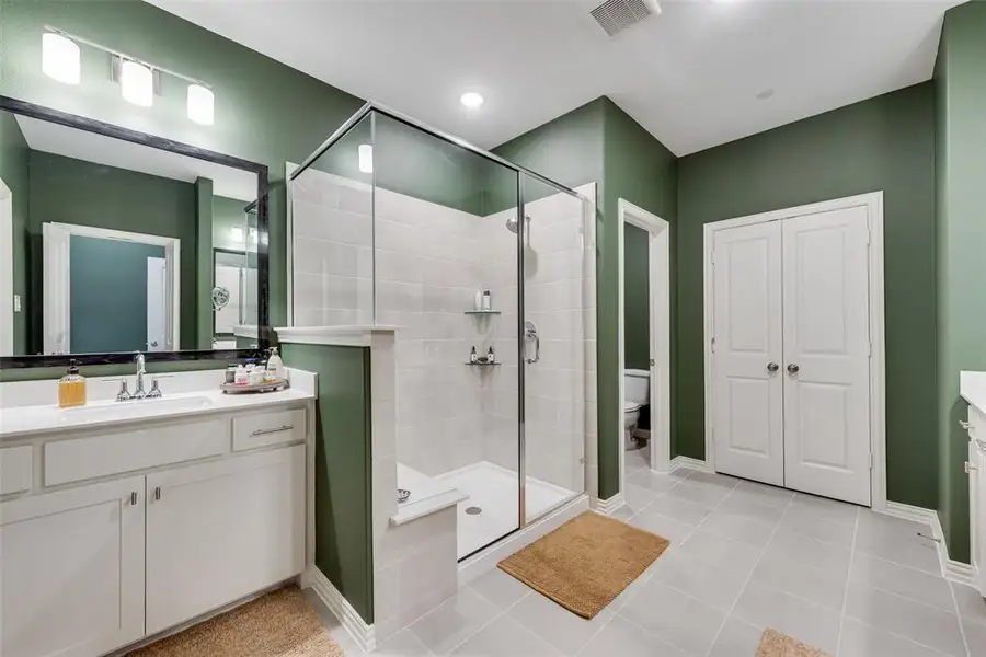 Glass-enclosed shower with subway tile surround, tile flooring, dual vanities with white cabinetry, and a large upgraded framed mirror with integrated lighting Glass-enclosed shower with subway tile surround, tile flooring, dual vanities with white cabinetry, and a large upgraded framed mirror with integrated lighting