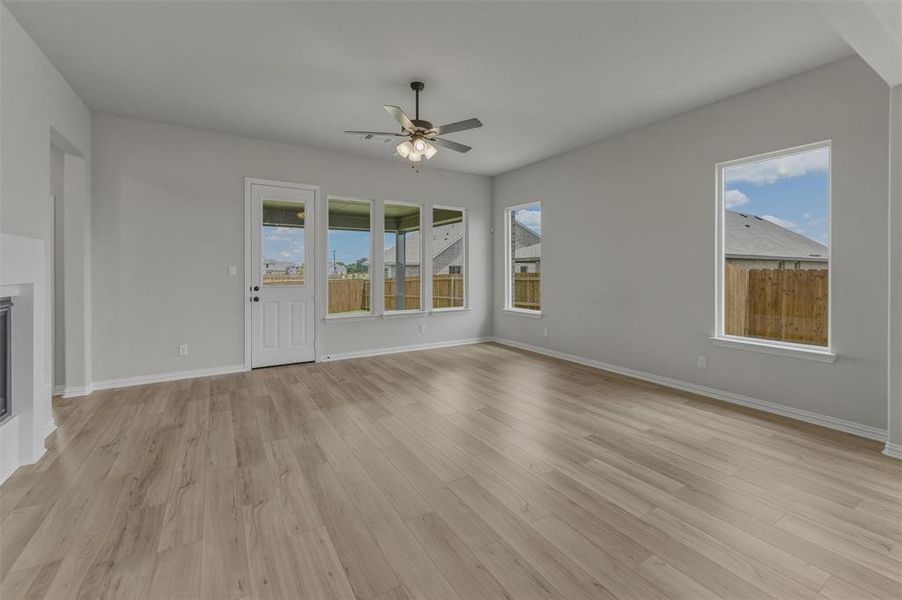 Spacious living area featuring contemporary wood-finish flooring, a ceiling fan with integrated lighting, and multiple windows for abundant illumination Spacious living area featuring contemporary wood-finish flooring, a ceiling fan with integrated lighting, and multiple windows for abundant illumination
